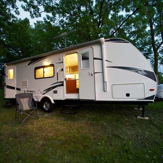 travel trailer surrounded by trees, with door open and lights on inside