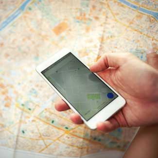 hand holding a cell phone navigating a map with image of map in background